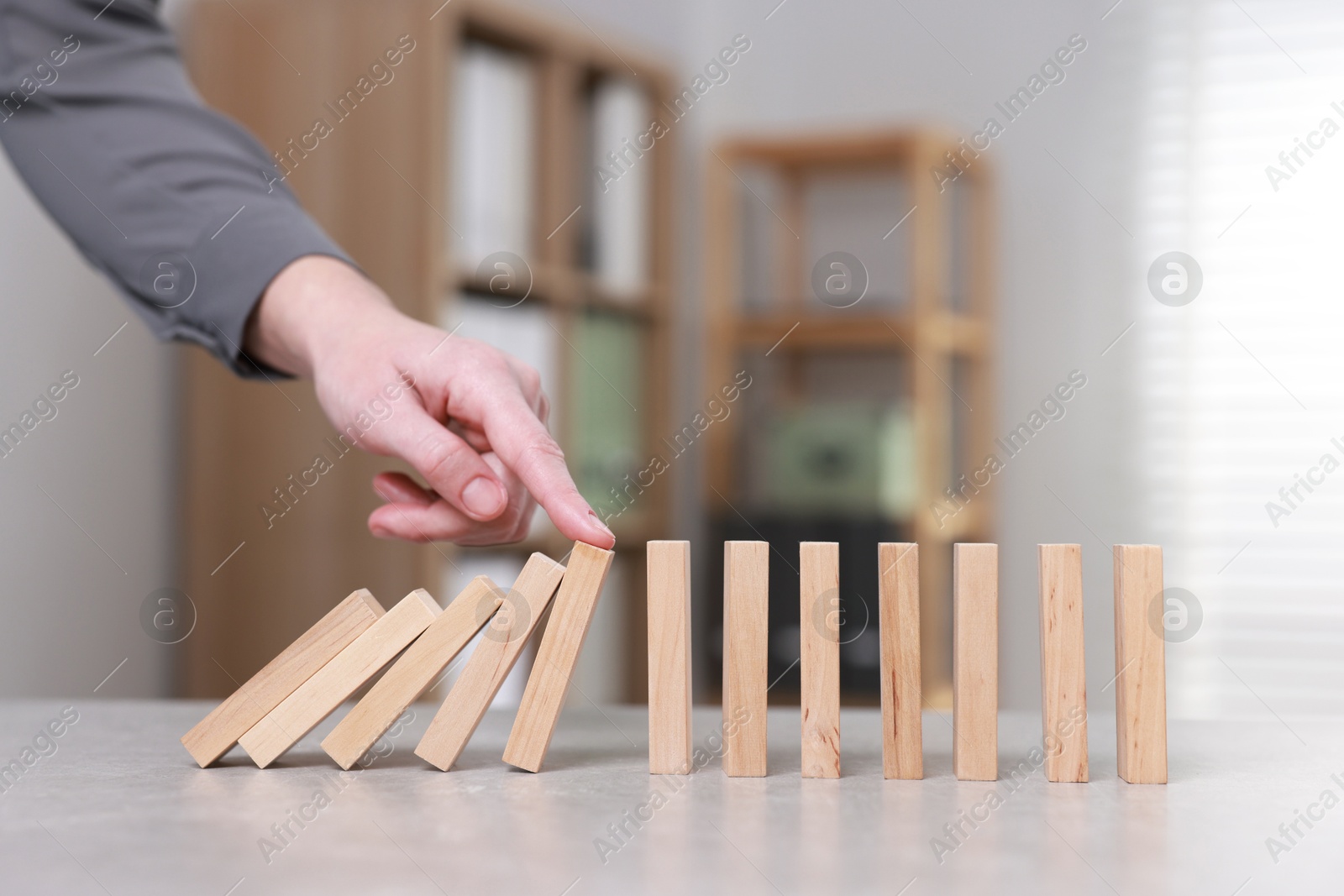 Photo of Woman stopping wooden blocks from falling at table, closeup. Domino effect