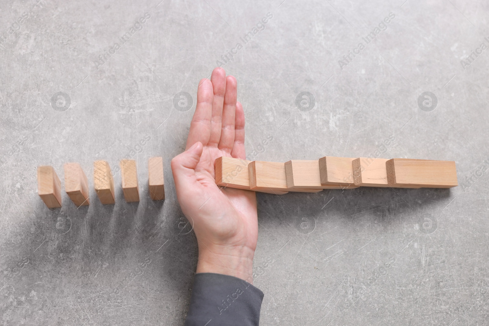 Photo of Woman stopping wooden blocks from falling on grey background, top view. Domino effect