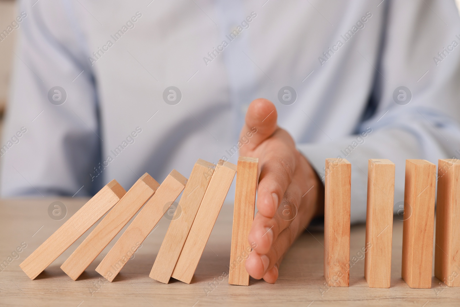 Photo of Man stopping wooden blocks from falling at table, closeup. Domino effect