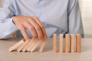 Photo of Man stopping wooden blocks from falling at table, closeup. Domino effect