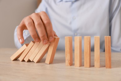 Photo of Man stopping wooden blocks from falling at table, closeup. Domino effect