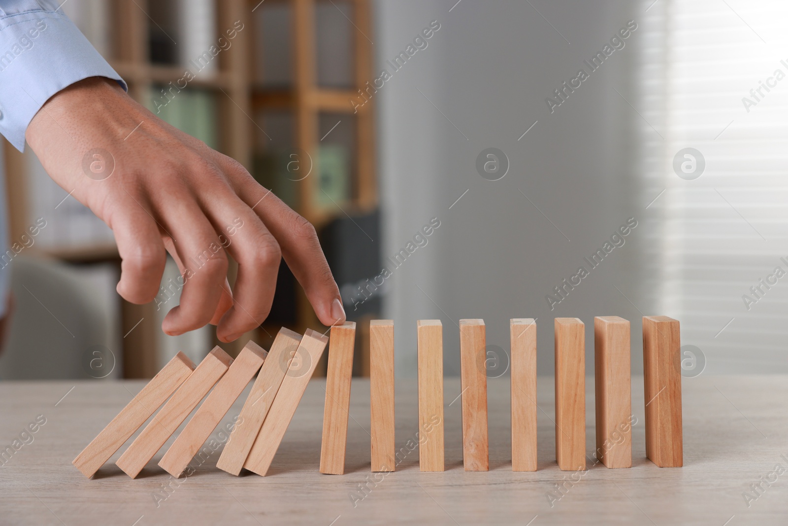 Photo of Man stopping wooden blocks from falling at table, closeup. Domino effect