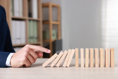 Photo of Domino effect. Man pushing wooden blocks at table, closeup