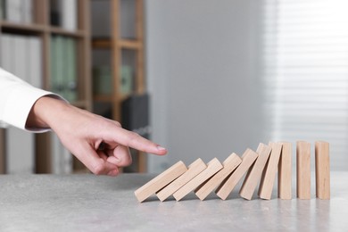 Photo of Domino effect. Man pushing wooden blocks at table, closeup