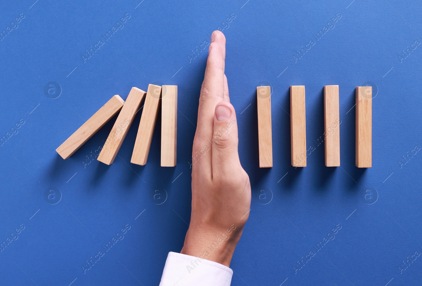 Photo of Man stopping wooden blocks from falling on blue background, top view. Domino effect