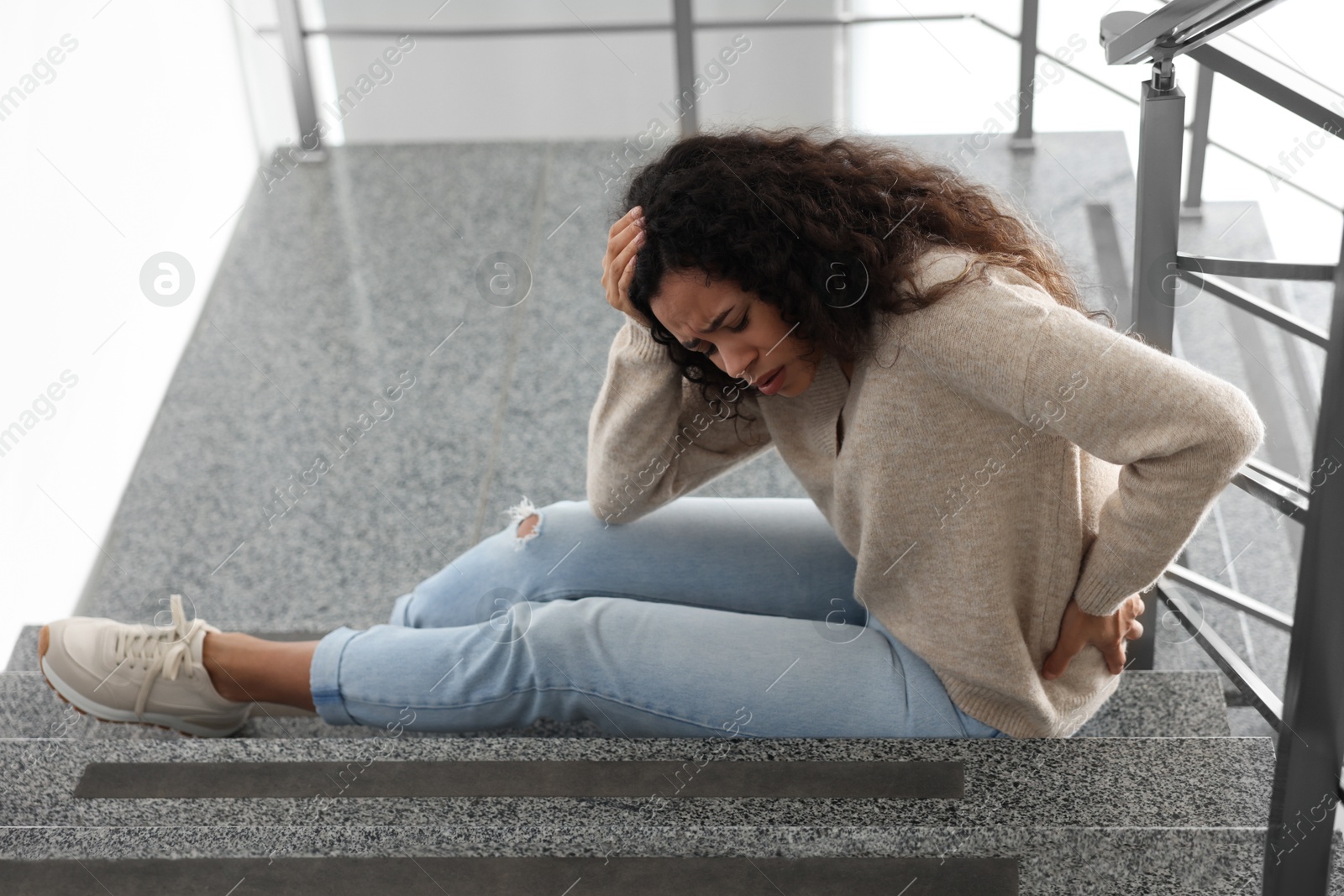 Photo of Woman with injured head and back on stairs in building after fall. Dangerous accident