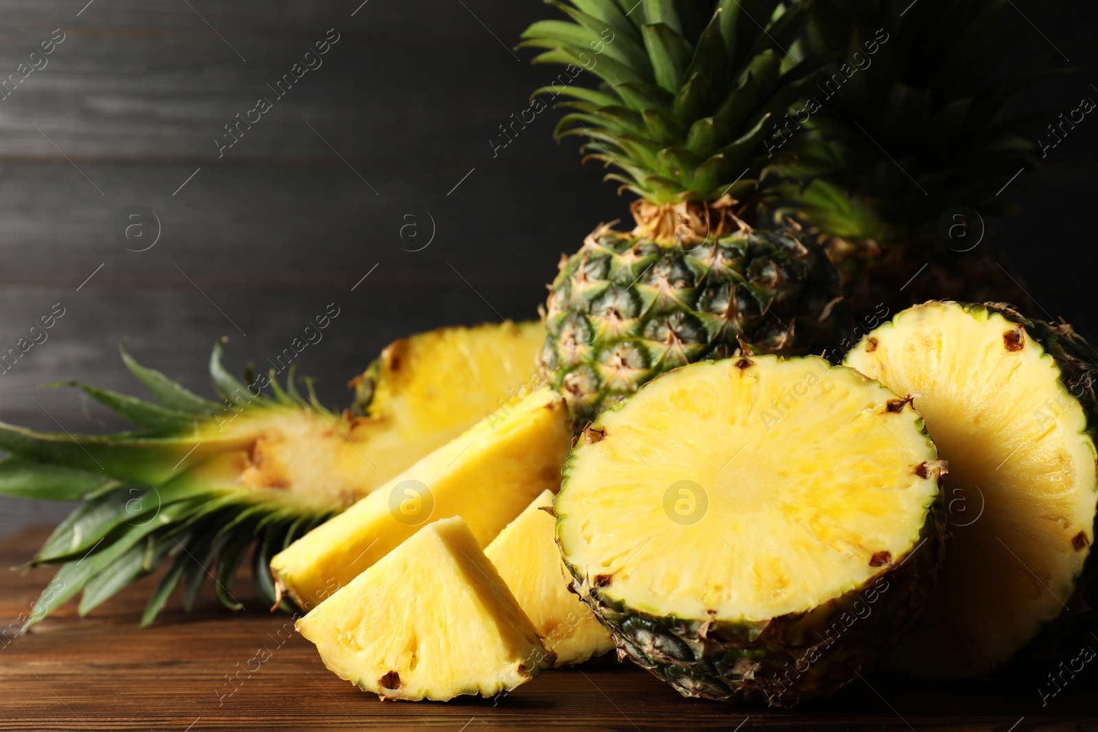 Photo of Whole and cut ripe pineapples on wooden table, closeup