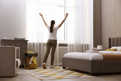 Photo of Traveller opening curtains in hotel room, back view