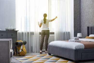 Photo of Traveller opening curtains in hotel room, back view