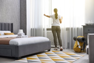 Photo of Traveller opening curtains in hotel room, back view