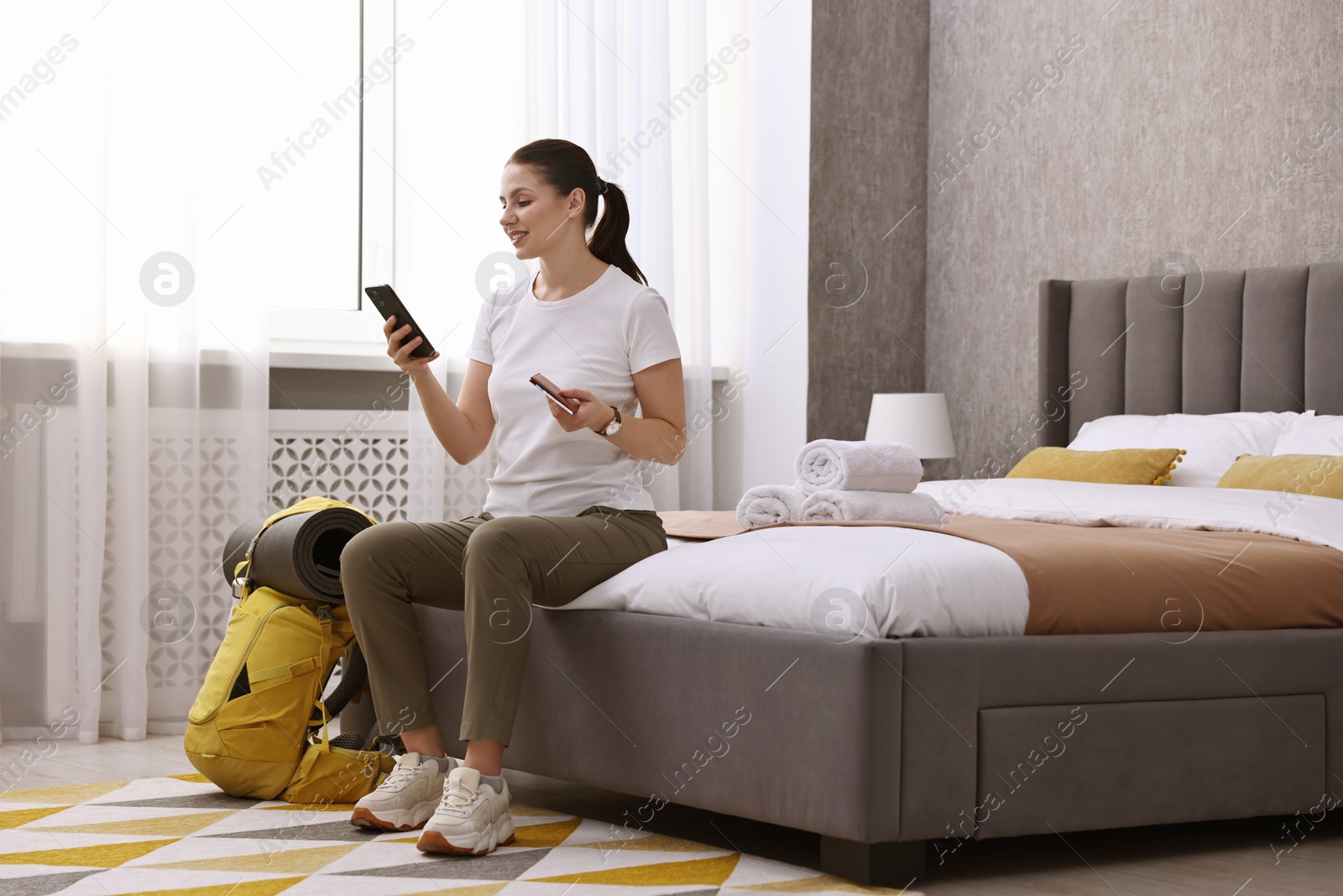 Photo of Traveller with phone, passport and backpack sitting on bed in hotel room