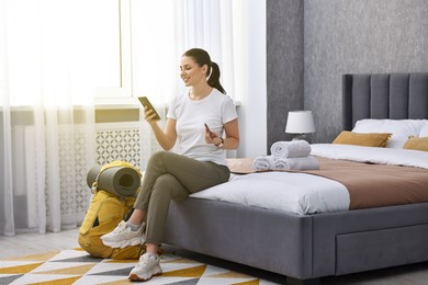 Photo of Traveller with phone, passport and backpack sitting on bed in hotel room