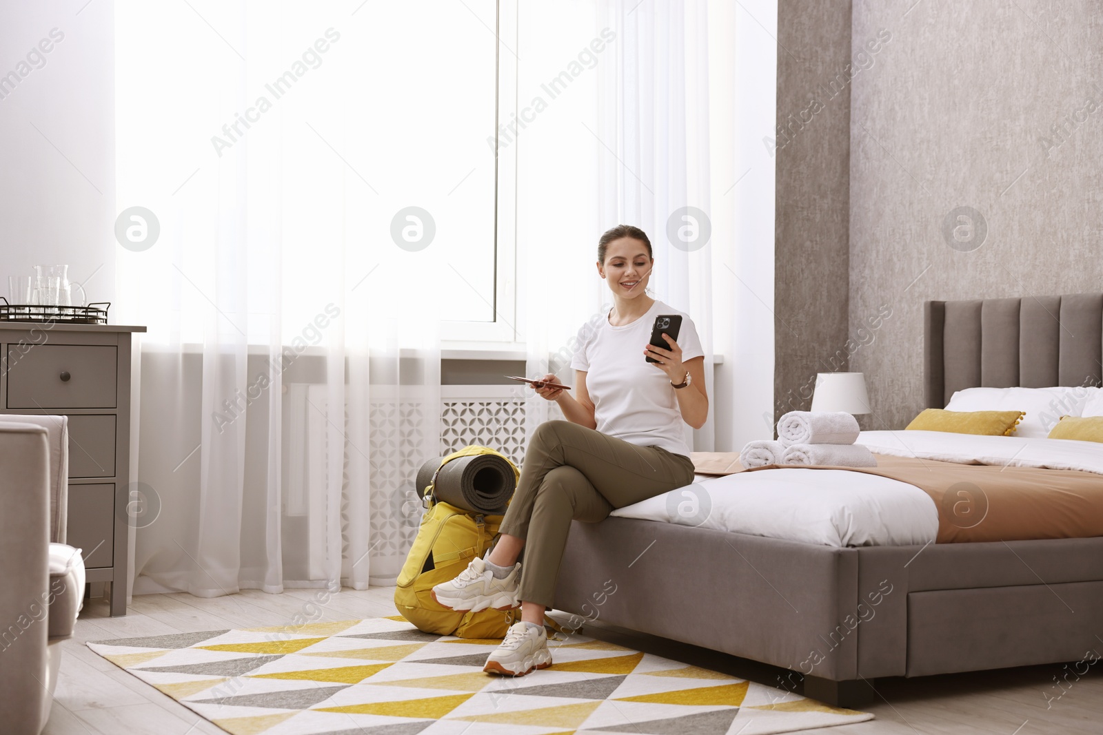 Photo of Traveller with phone, passport and backpack sitting on bed in hotel room