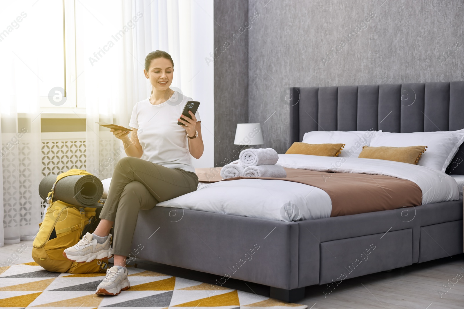 Photo of Traveller with phone, passport and backpack sitting on bed in hotel room