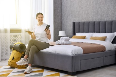 Photo of Traveller with phone, passport and backpack sitting on bed in hotel room