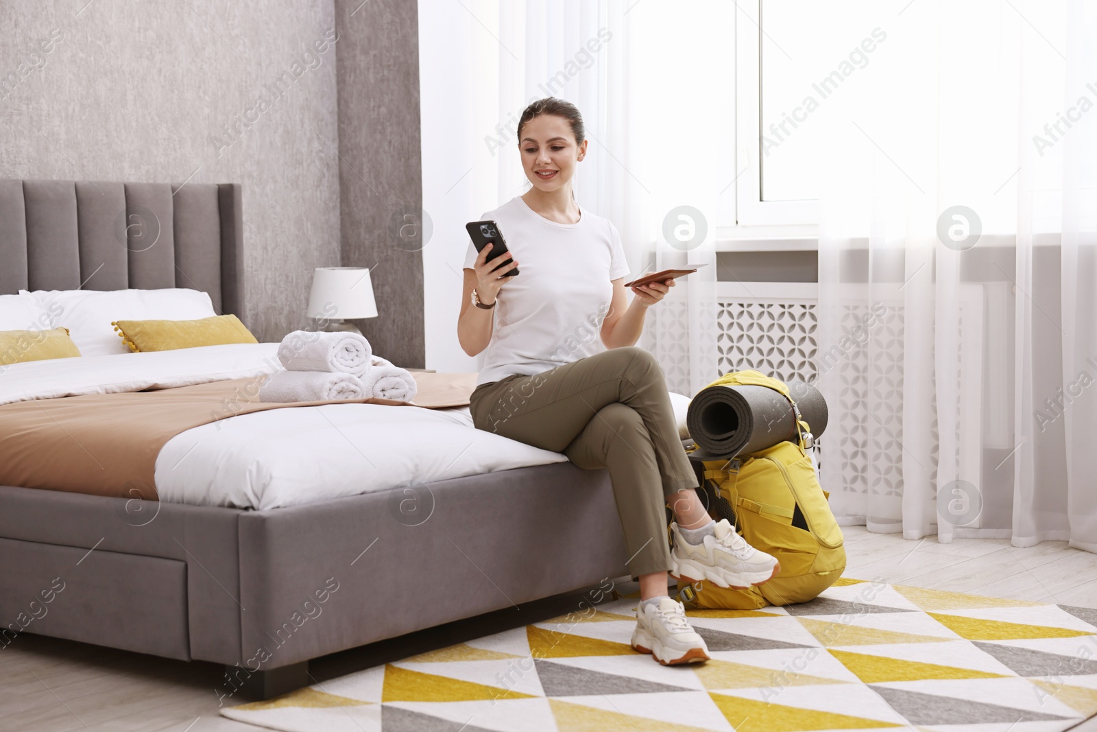 Photo of Traveller with phone, passport and backpack sitting on bed in hotel room