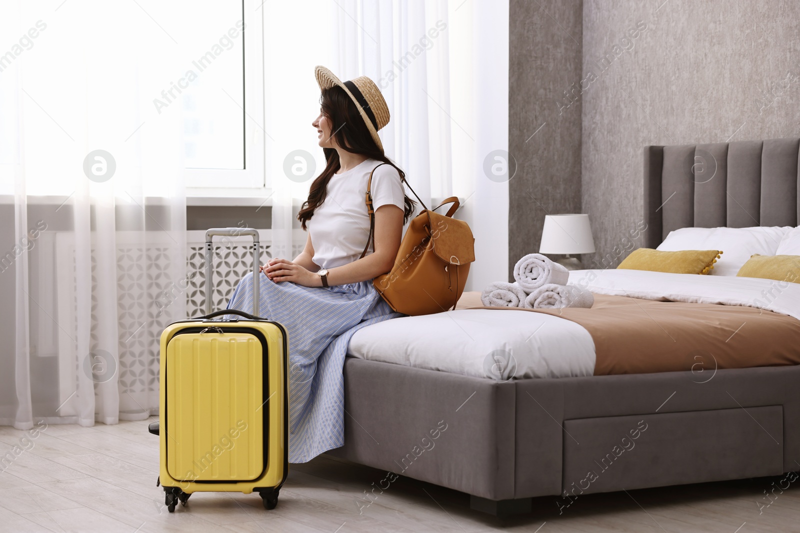 Photo of Traveller with suitcase sitting on bed in hotel room