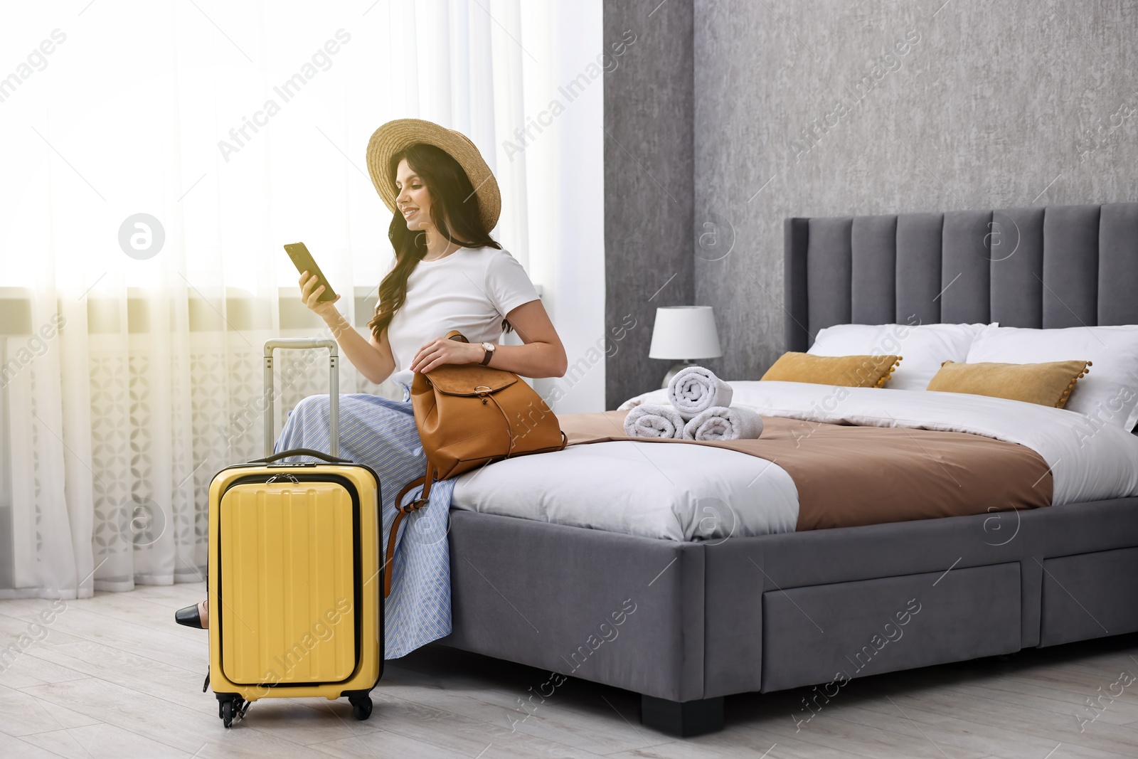 Photo of Traveller with phone and suitcase sitting on bed in hotel room