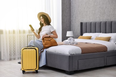 Photo of Traveller with phone and suitcase sitting on bed in hotel room