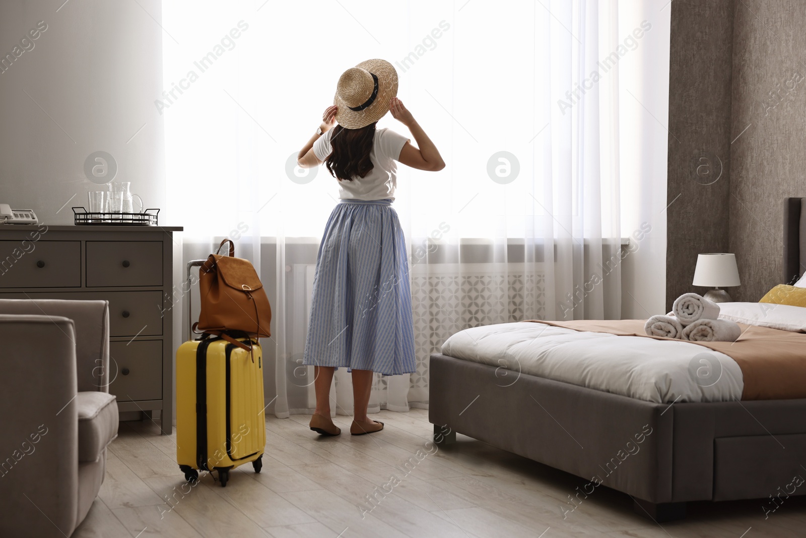 Photo of Traveller with suitcase standing near window in hotel room, back view