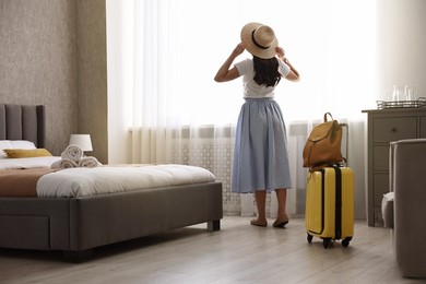 Photo of Traveller with suitcase standing near window in hotel room, back view