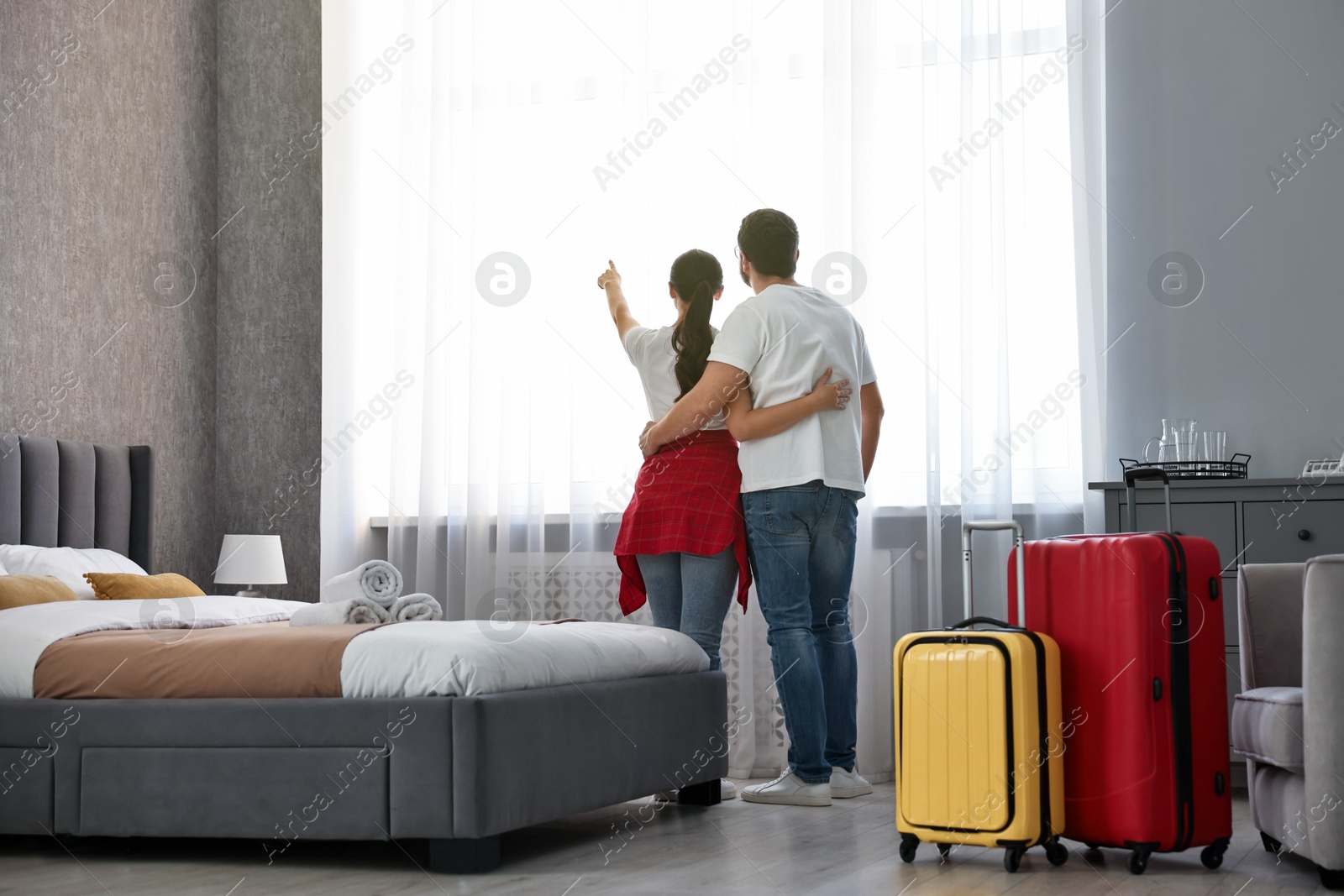 Photo of Travellers with suitcases standing near window in hotel room, back view