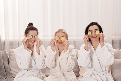 Photo of Happy women with cucumber slices on sofa in spa