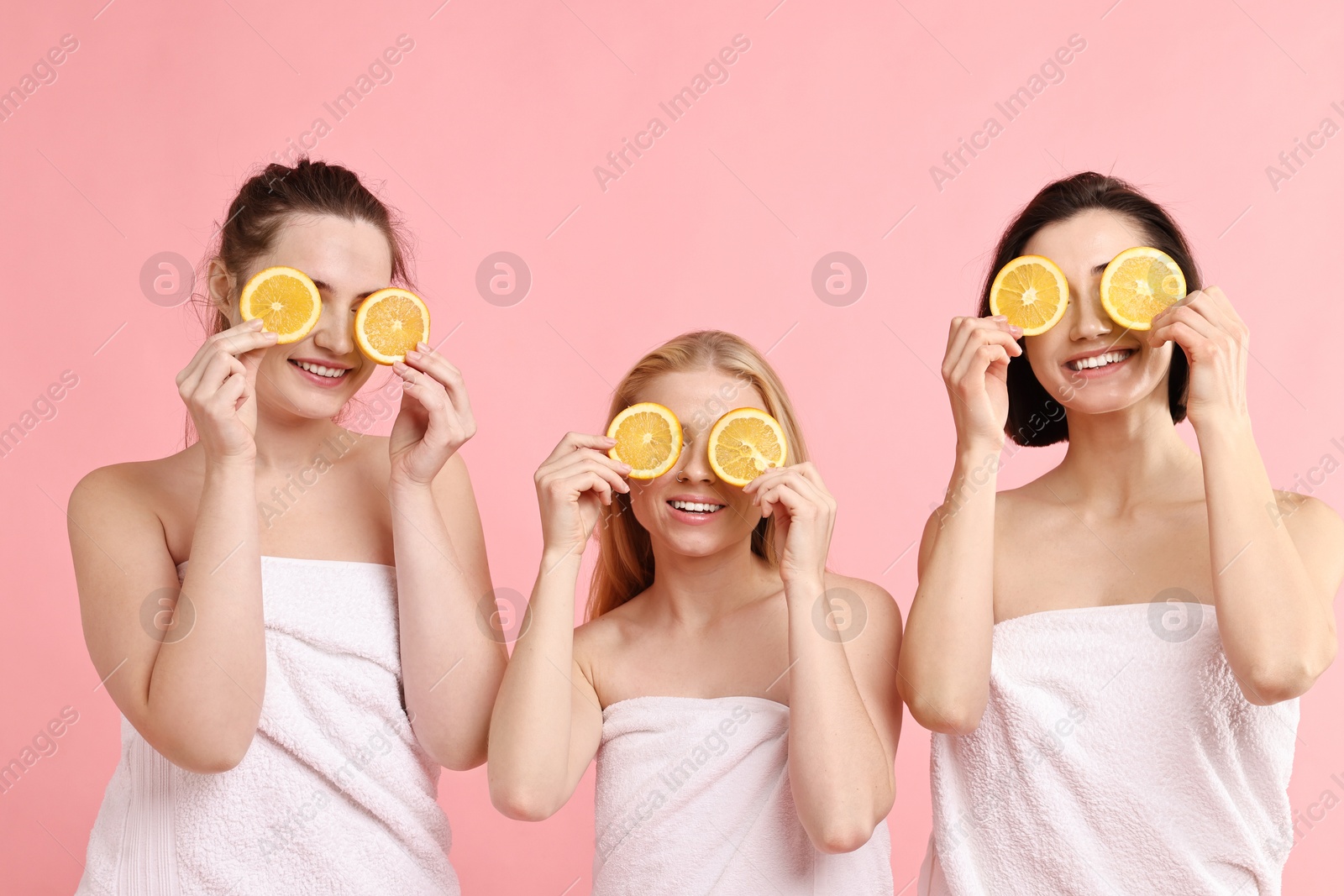 Photo of Spa day. Cheerful women wrapped in towels with orange slices on pink background