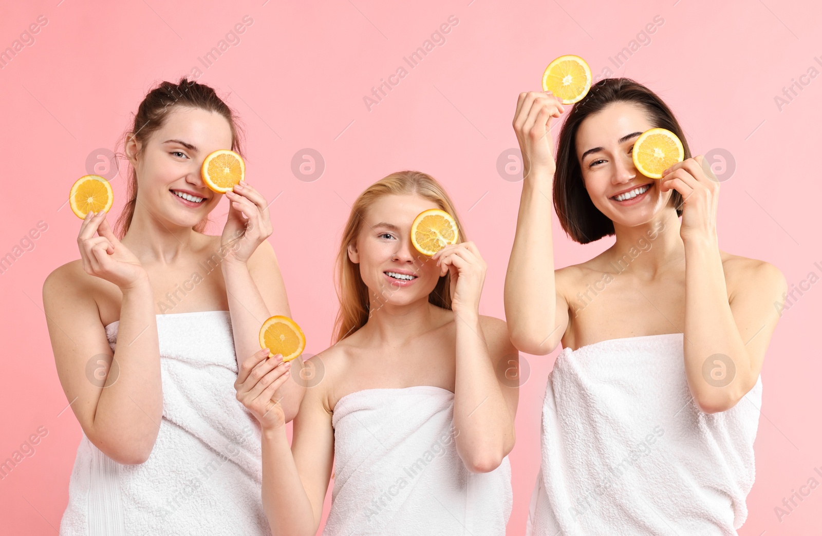 Photo of Spa day. Cheerful women wrapped in towels with orange slices on pink background