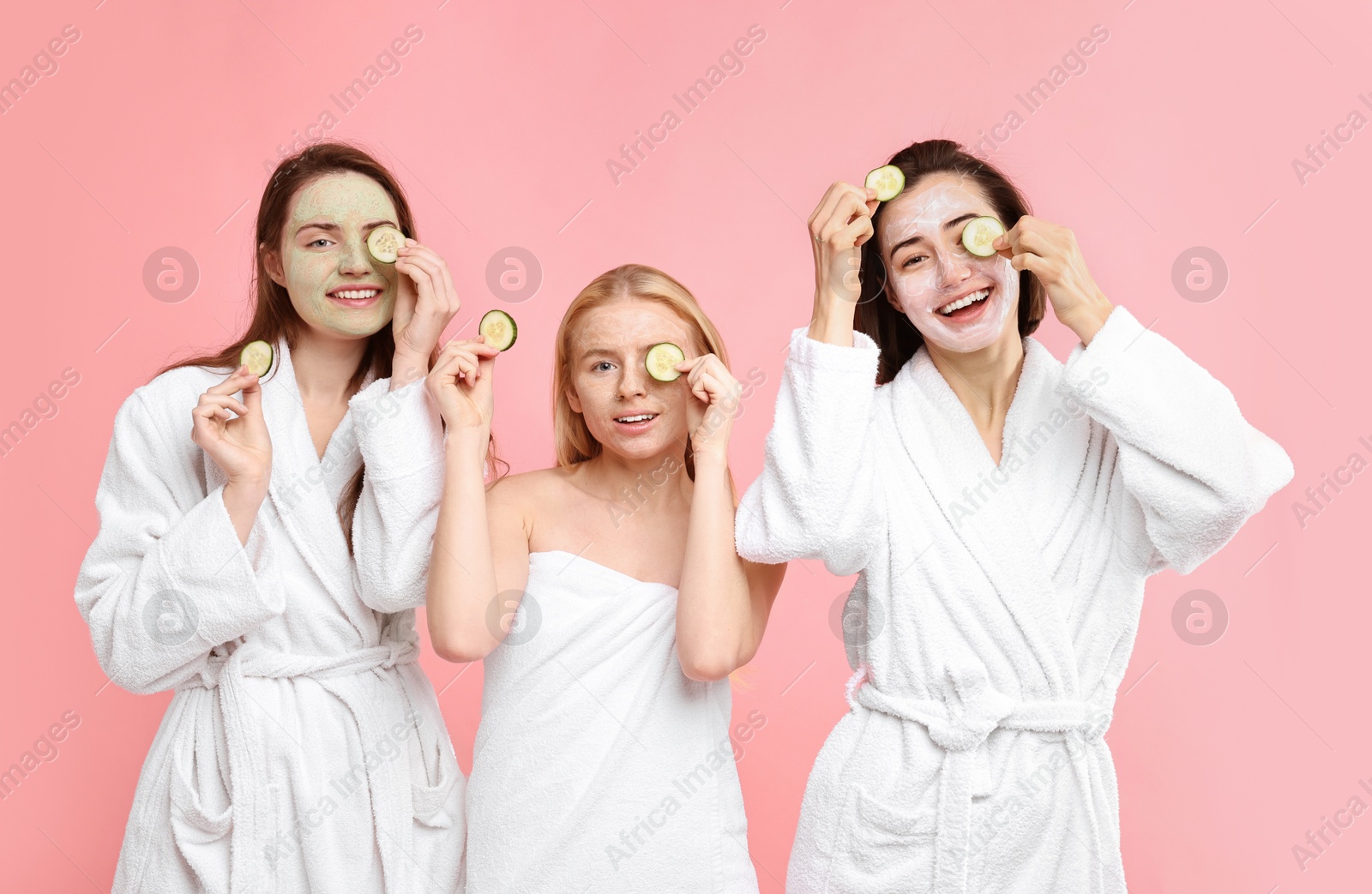 Photo of Spa day. Happy women with face masks and cucumber slices on pink background