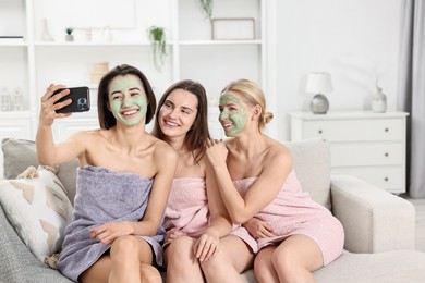 Photo of Spa day. Beautiful women with face masks taking selfie on sofa indoors