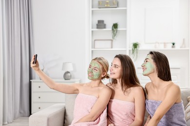 Spa day. Beautiful women with face masks taking selfie on sofa indoors