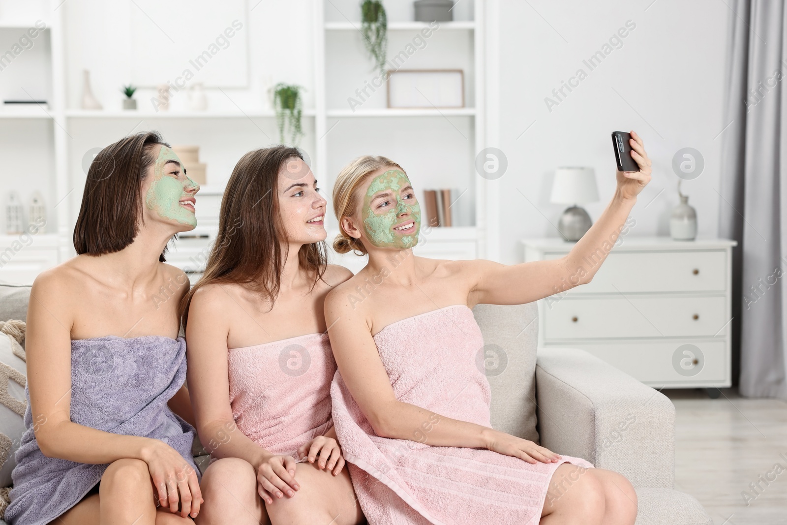 Photo of Spa day. Beautiful women with face masks taking selfie on sofa indoors