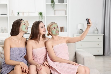 Photo of Spa day. Beautiful women with face masks taking selfie on sofa indoors