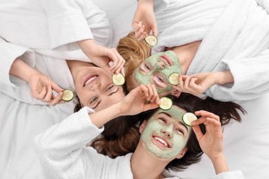 Spa day. Beautiful woman with face masks and cucumber slices on bed, above view