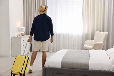 Photo of Traveller with suitcase in hotel room, back view