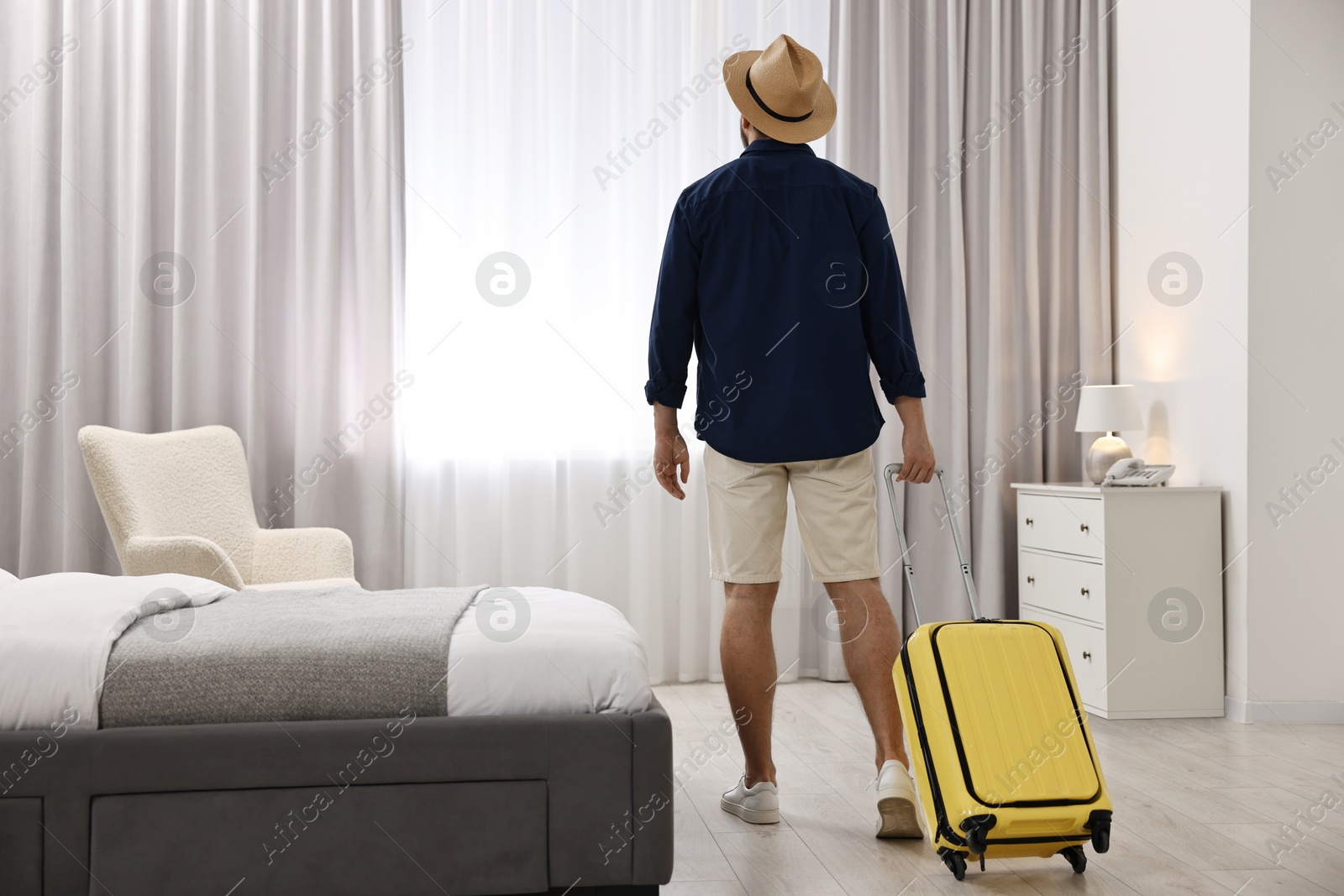 Photo of Traveller with suitcase in hotel room, back view