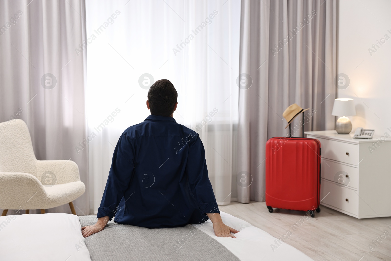 Photo of Traveller sitting on bed in hotel room, back view