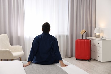 Photo of Traveller sitting on bed in hotel room, back view