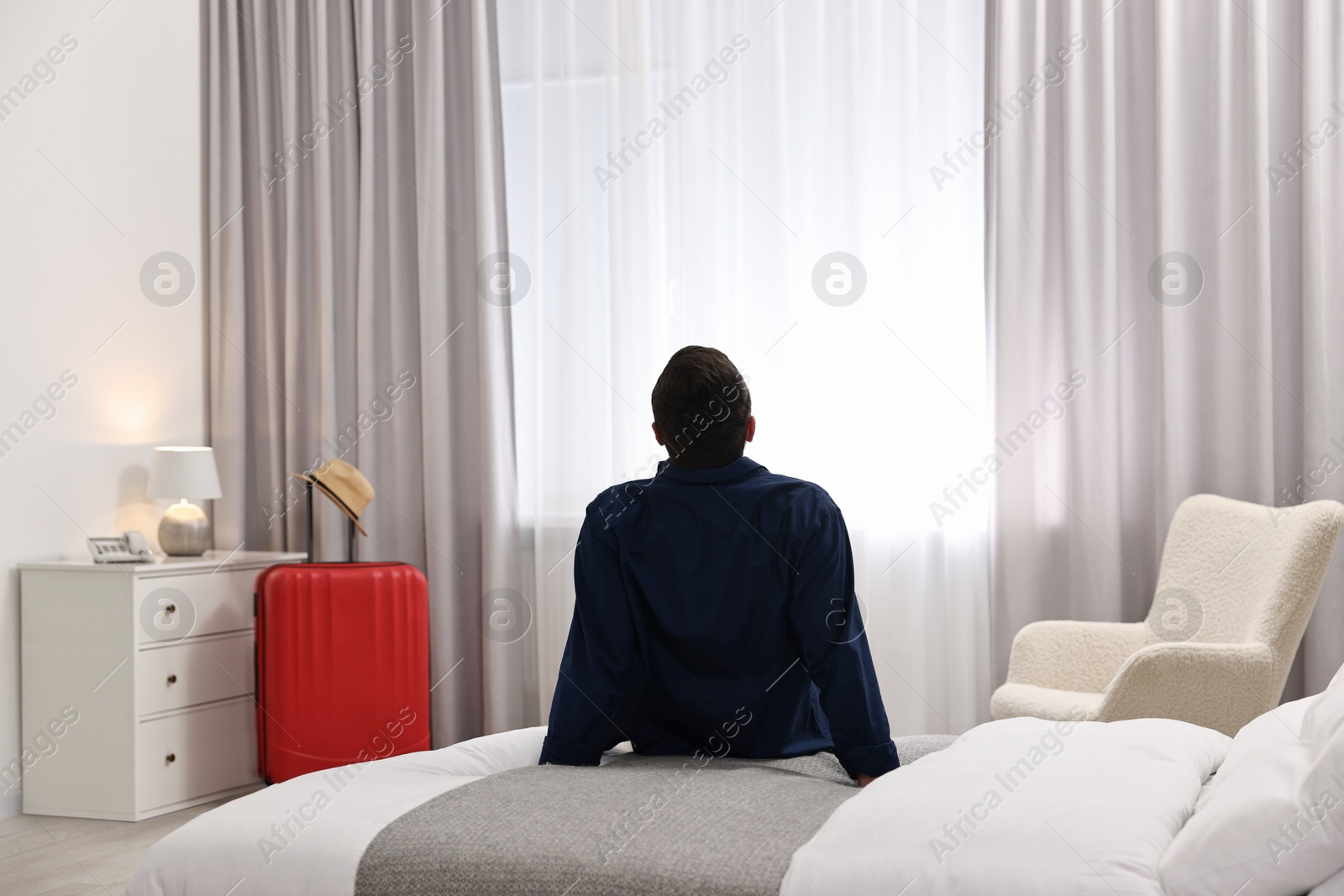 Photo of Traveller sitting on bed in hotel room, back view