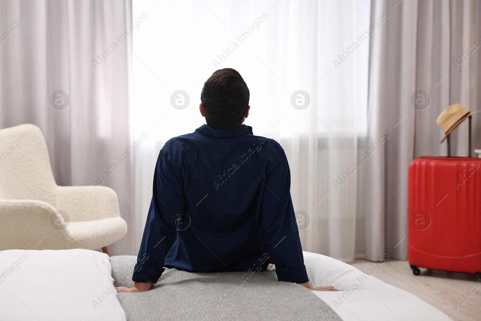 Photo of Traveller sitting on bed in hotel room, back view