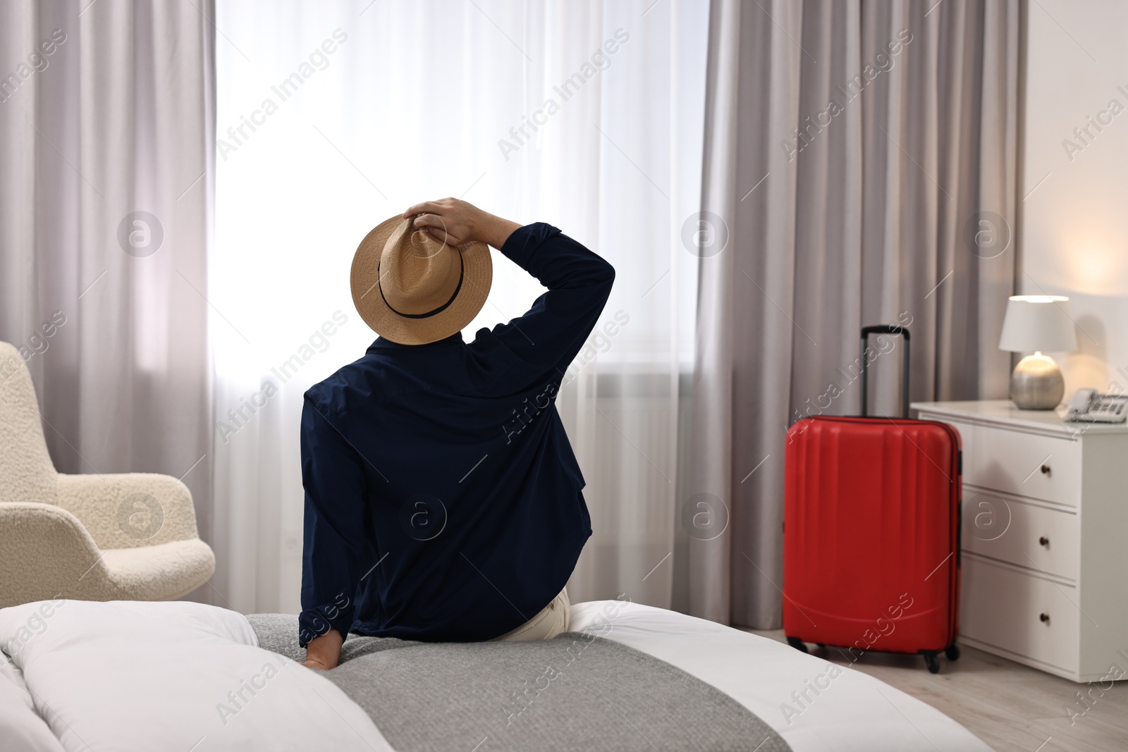 Photo of Traveller sitting on bed in hotel room, back view