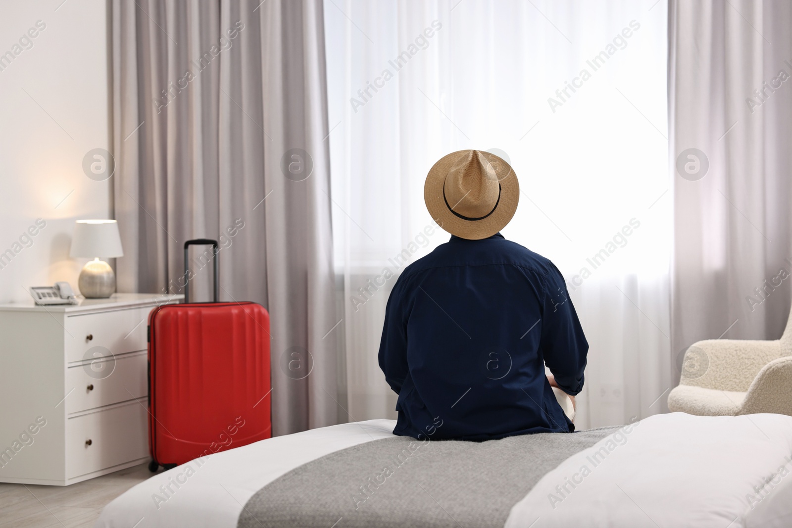 Photo of Traveller sitting on bed in hotel room, back view