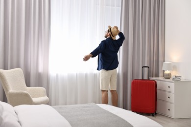 Photo of Traveller and suitcase near window in hotel room, space for text