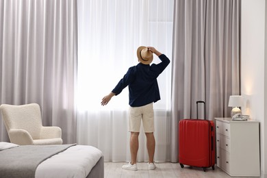 Photo of Traveller and suitcase near window in hotel room, back view