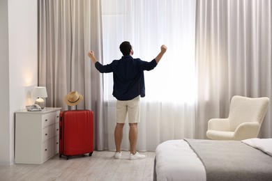 Photo of Traveller and suitcase near window in hotel room, back view