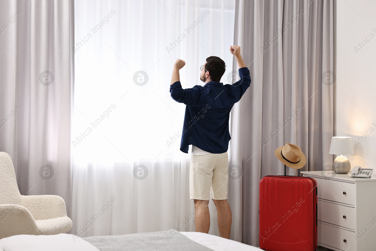 Photo of Traveller and suitcase near window in hotel room, space for text