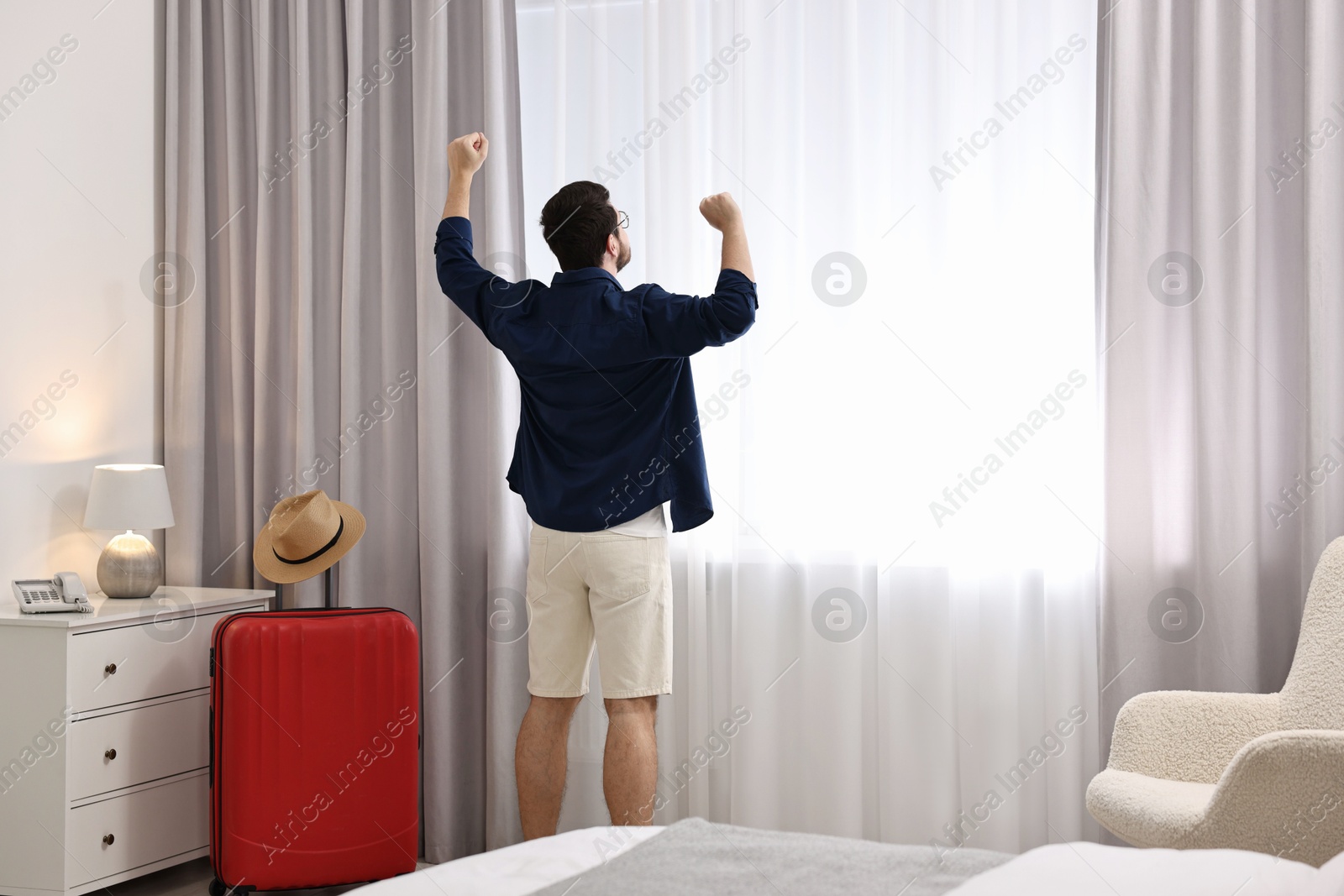 Photo of Traveller and suitcase near window in hotel room, space for text