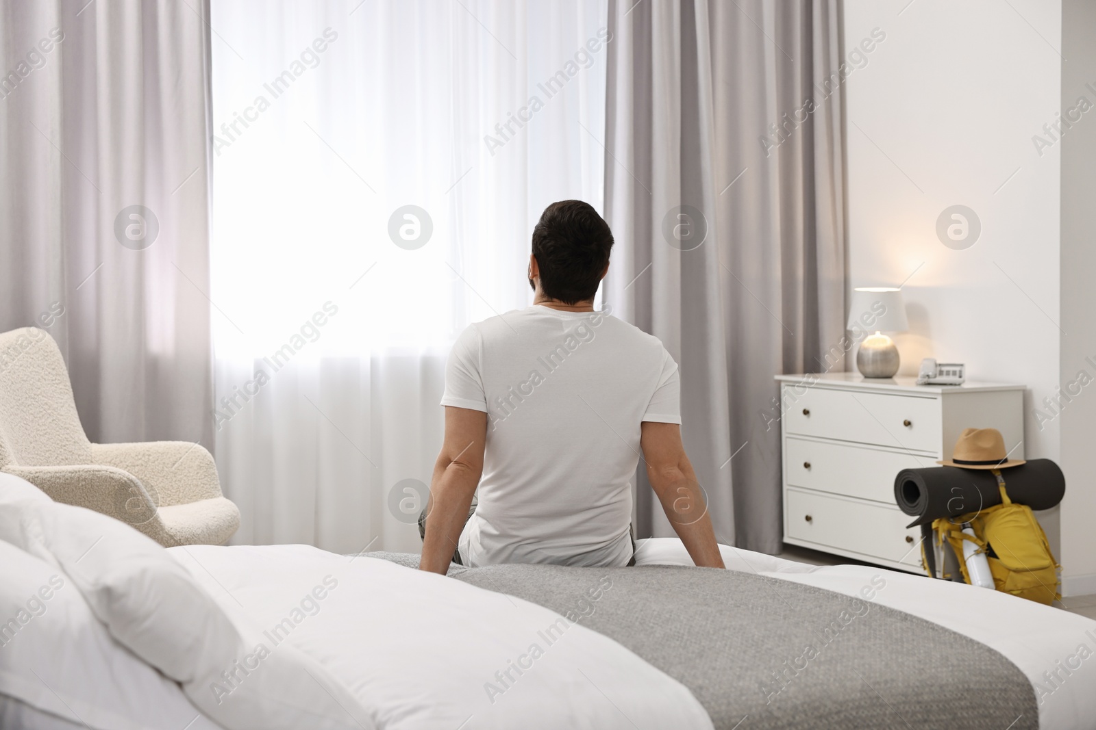 Photo of Traveller sitting on bed in hotel room, back view