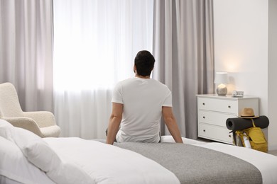 Traveller sitting on bed in hotel room, back view